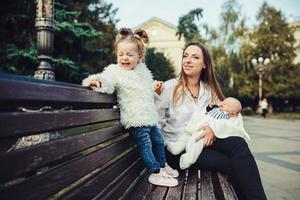 Mutter und zwei Töchter ruhen auf einer Bank foto