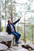 Der Typ sitzt im Wald auf einem Felsen foto