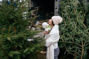 frau mit einem weißen hund in ihren armen in der nähe von grünen weihnachtsbäumen foto