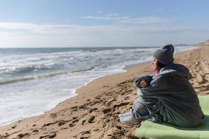 hübsche Frau in warmer Kleidung, die am kalten Herbststrand sitzt. foto