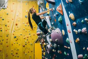 junge Frau, die eine hohe, künstliche Kletterwand im Innenbereich erklimmt foto