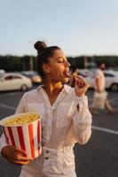 Junge süße Frau, die Popcorn auf einem Parkplatz eines Einkaufszentrums hält foto