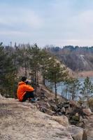 Ein junger Mann, der am Rand einer Klippe sitzt, posiert für die Kamera foto