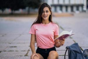 Fröhliche junge Frau, die sich Notizen macht, während sie auf Stufen im Freien sitzt foto