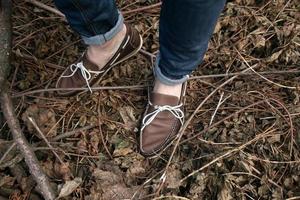 Füße des Mannes in den authentischen Stiefeln und Selvedge-Jeans, auf dem Hintergrund von Zweigen foto