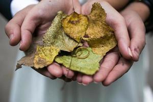 braut und bräutigam, die hochzeitsringe und herbstblätter in den händen halten foto