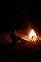 Frau, die am Lagerfeuer im Nachtwald sitzt und sich erwärmt. foto