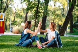 Fröhliche Freundinnen, die die Hände hochheben und im Stadtpark High Five geben foto