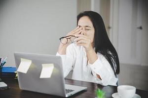 junge geschäftsfrau person schläfrig und hat frustration augenprobleme mit kopfschmerz durch die verwendung eines laptops auf ihrem schreibtisch. gestresste mitarbeiterin müde und erschöpft von überarbeitung. foto