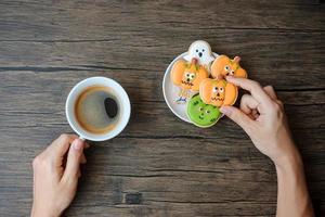 Hand, die eine Kaffeetasse hält, während sie lustige Halloween-Kekse isst. glücklicher halloween-tag, trick oder bedrohung, hallo oktober, herbstherbst, traditionelles, party- und feiertagskonzept foto