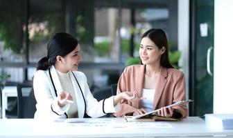 zwei junge asiatische geschäftsfrauen diskutieren die arbeits- und planungsstrategie für investitionsprojekte. geschäftsleute, die zusammen mit laptop-computer im büro sprechen. foto