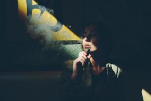 Mädchen sitzt und raucht elektronische Zigarette foto
