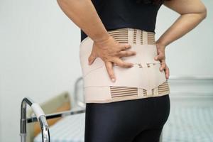 asiatische Patientin mit Rückenschmerzen-Unterstützungsgurt für orthopädische Lendenwirbelsäule. foto