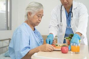 asiatische senior oder ältere alte damenpatientin, die frühstück und gemüse gesundes essen mit hoffnung und glücklich isst, während sie im krankenhaus sitzt und hungrig auf dem bett sitzt. foto