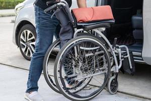 asiatische Frau, die den Rollstuhl in ihr Auto faltet und anhebt. Konzept der Barrierefreiheit. foto