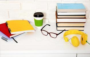 arbeitsplatz- und bildungszubehör auf dem tisch. Tasse Kaffee, Bücher, Gläser, Notizbücher, Kopfhörer. Bildung aufhalten foto