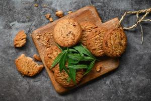 Cannabis-Lebensmittelkekse mit Cannabisblatt-Marihuana-Kraut auf Holz- und dunklem Hintergrund, köstlicher süßer Dessert-Keks mit Hanfblattpflanze thc cbd-Kräuter-Nahrungsmittelsnack und Medizin foto