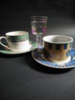 teetasse, kaffeetasse und transparentes glas mit obstmuster, gefüllt mit mineralwasser auf schwarzem hintergrund. foto