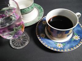 teetasse, kaffeetasse und transparentes glas mit obstmuster, gefüllt mit mineralwasser auf schwarzem hintergrund. foto