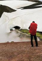 Wanderer mit roter Rucksackabdeckung, der vor einem Gletscher in Island steht foto