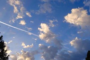 blauer himmel, sonnige wolken und der weiße flugzeugkondensstreifen, morgendlicher wolkenhintergrund, flugzeugfliegen in den flauschigen wolken, schönheit des wetters. foto