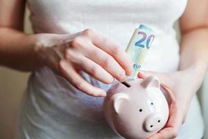 Frauenhände, die rosa Sparschwein halten und Geld Euro setzen. sparen investitionsbudget geschäftsvermögen ruhestand finanzgeld bankkonzept. foto