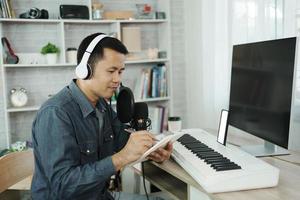 asiatischer mann mit weißen kopfhörern komponiert lieder und lernt online oder nimmt ton mit einem mikrofon auf und verwendet ein computeraufzeichnungsmusikprogramm. toningenieur mann musik aufnehmen. foto