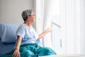 asiatischer geduldiger mann, der nach draußen schaut und auf dem krankenhausbett im krankenzimmer sitzt. foto