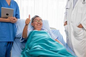 asiatischer geduldiger mann, der im krankenzimmer auf dem krankenbett lächelt und sich hinlegt foto