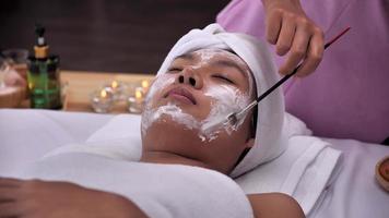 kosmetikerin verwendet crememaske auf dem gesicht der jungen asiatischen frau mit bürste im spa-salon. foto