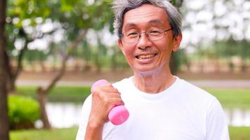 glücklicher asiatischer mann, der übung macht, indem er hanteln im park anhebt. foto