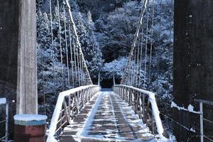 Holz- und Metallbrücke über ein Flusstal im Schnee von vorne foto