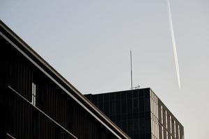 Kondensstreifen am hellblauen Himmel über modernen Gebäuden foto