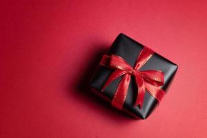 Draufsicht auf schwarze Geschenkbox mit roten und schwarzen Bändern isoliert auf rotem Hintergrund. foto