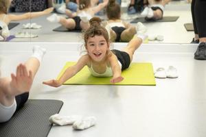 Kind trainiert im Fitnessstudio auf der Matte, macht Dehnübungen und Bauchmuskeln, Gymnastik und allgemeines körperliches Sporttraining. Seit der Kindheit an sich und seinem Körper arbeiten, sich selbst überwinden foto