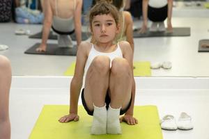 Kind trainiert im Fitnessstudio auf der Matte, macht Dehnübungen und Bauchmuskeln, Gymnastik und allgemeines körperliches Sporttraining. Seit der Kindheit an sich und seinem Körper arbeiten, sich selbst überwinden foto