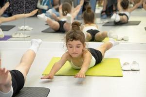 Kind trainiert im Fitnessstudio auf der Matte, macht Dehnübungen und Bauchmuskeln, Gymnastik und allgemeines körperliches Sporttraining. Seit der Kindheit an sich und seinem Körper arbeiten, sich selbst überwinden foto