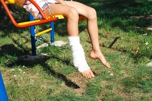 Kinderbeine werden mit Gips verbunden - barfuß auf einer Schaukel. traumatische Ausrüstung, Kinderverletzung, Prellung, Verstauchung, Fraktur foto