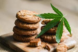 Cannabis-Lebensmittelkekse mit Cannabisblatt-Marihuana-Kraut auf Holzhintergrund, köstlicher süßer Dessert-Keks mit Hanfblattpflanze thc cbd-Kräuter-Nahrungsmittelsnack und Medizin foto