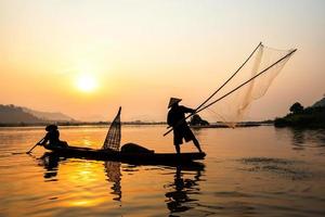 Asien-Fischernetz mit auf Holzboot Casting net Sonnenuntergang oder Sonnenaufgang im Mekong-Fluss - Silhouette Fischer foto