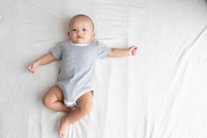 Draufsicht und Seitenbereich Baby trägt ein gestreiftes Hemd und spreizt Arme und Beine auf einem weißen Teppich. foto