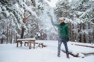 gutaussehender positiver mann hält hand auf tanne, sieht mit fröhlichem ausdruck aus, genießt schönheit von schneebedeckten bäumen, verbringt wochenenden im wald. lächelnder bärtiger Mann, der gute Laune hat foto