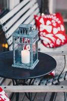 vertikale Aufnahme eines gemütlichen Cafés im Freien mit Holzbank und Kissen, Kerzenlicht für Ihre Erholung. kleine brennende kerze in lampe auf rundem tisch foto