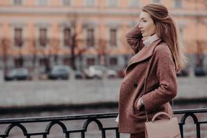 bmodischer mantel, schöne frau in stylischem mantel, hält hand in der tasche, konzentriert sich auf distanz, geht in der stadt spazieren, denkt an etwas, hat gute ruhe. Menschen und Lifestyle-Konzept. foto