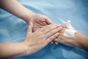 Nahaufnahme der Patientenhand im Bett, wobei eine Hand gehalten wird, um im Krankenhaus zu unterstützen foto