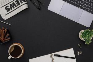 kreatives flatlay von büromaterialmodell mit notizbuch, heißer kaffeetasse, gläsern, büchern, zeitung und zubehör auf schwarzem schreibtisch mit kopierraum, arbeitsbereich für freiberuflerhintergrund foto