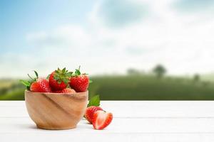 Rote Erdbeeren mit Blättern in einer Holzschale auf dem Holztisch und dem Plantagenhintergrund foto