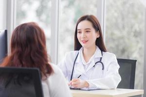 asiatische frau, die einen medizinischen mantel und ein stethoskop trägt, spricht mit einer patientin, um gesundheitsinformationen im krankenhaus zu konsultieren und vorzuschlagen. foto