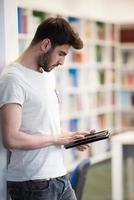 Student in der Schulbibliothek mit Tablet für die Recherche foto