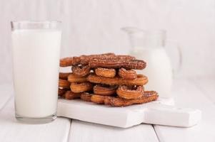 Hausgemachte Churros mit Milch und Sahne auf weißem Holzhintergrund. foto